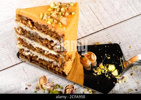 Torta server con pezzo di deliziosa torta di carote con pistacchi su tavolo di legno Foto Stock