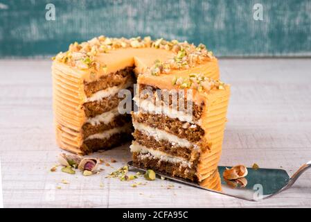 Torta server con pezzo di deliziosa torta di carote con pistacchi su tavolo di legno Foto Stock