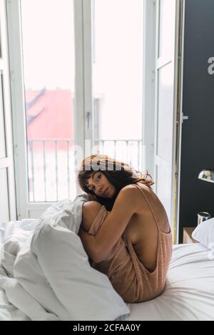 Giovane donna pigra in piumino seduta sul letto in camera da letto Foto Stock