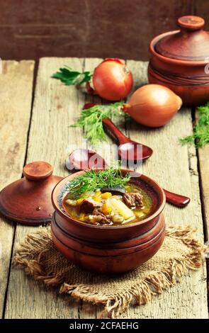 Zuppa con funghi, manzo e orzo, pentole di argilla, sfondo di legno d'annata, fuoco selettivo Foto Stock