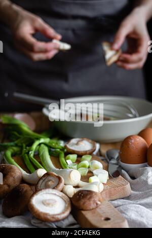 Mazzetto di scalioni freschi e funghi posto sul tagliere vicino uova e semi di papavero contro raccolto casalinga mescolando ingredienti nel recipiente Foto Stock