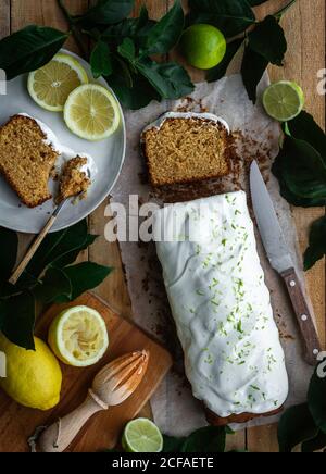 Vista dall'alto della focaccia di deliziosa pasticceria con la ciliegina sulla torta posto su tavolo di legno vicino utensili da cucina e limoni maturi e. lime Foto Stock