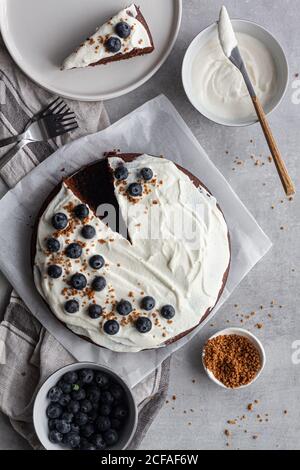 Dall'alto si può ammirare un piatto con gustoso cioccolato fatto in casa torta decorata con panna bianca vicino a una piccola fetta di torta e mirtilli messi a tavola in cucina Foto Stock