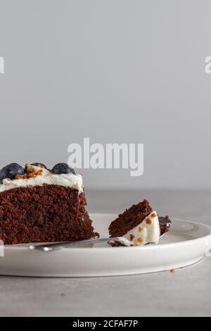 Fetta di pan di Spagna di cioccolato fatto in casa con panna montata fresca panna e mirtilli interi posti sul tavolo in cucina leggera Foto Stock