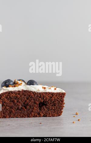 Fetta di pan di Spagna di cioccolato fatto in casa con panna montata fresca panna e mirtilli interi posti sul tavolo in cucina leggera Foto Stock