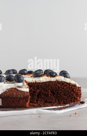 Fetta di pan di Spagna di cioccolato fatto in casa con panna montata fresca panna e mirtilli interi posti sul tavolo in cucina leggera Foto Stock