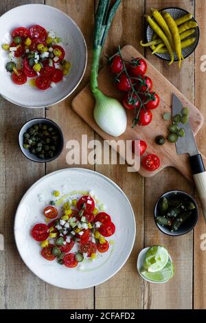 Vista dall'alto dei piatti con insalata di ciliegia fresca pomodori e cetrioli sottaceto con pepe caldo e scalogno e. posto su tavolo di legno vicino a calce schiacciata Foto Stock