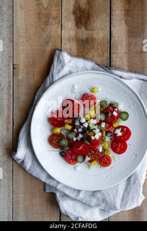 Vista dall'alto dei piatti con insalata di ciliegia fresca pomodori e cetrioli sottaceto con pepe caldo e scalogno e. posto su tavolo di legno vicino a calce schiacciata Foto Stock