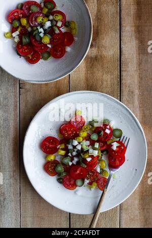 Vista dall'alto dei piatti con insalata di ciliegia fresca pomodori e cetrioli sottaceto con pepe caldo e scalogno e. posto su tavolo di legno vicino a calce schiacciata Foto Stock