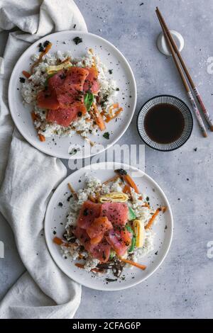 Da sopra gustoso appetitoso salmone affettato su riso bianco con verdure in piastra e bastoncini di legno sul tavolo Foto Stock