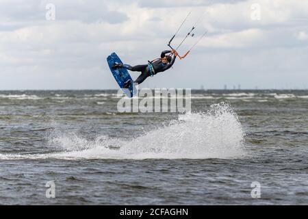 Malmo, Svezia - 23 agosto 2020: Un kitesurfer salta in alto in acqua in una giornata ventosa in cui molte persone cogliano l'opportunità di praticare sport acquatici Foto Stock