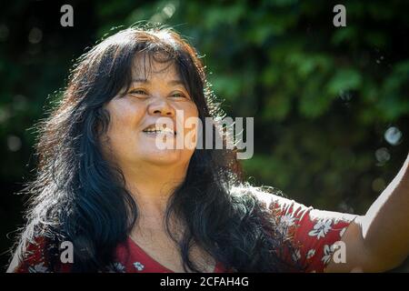Immagine closeup di una donna asiatica di mezza età, negli anni '50, con bolle di sapone. Foglie verdi sullo sfondo Foto Stock
