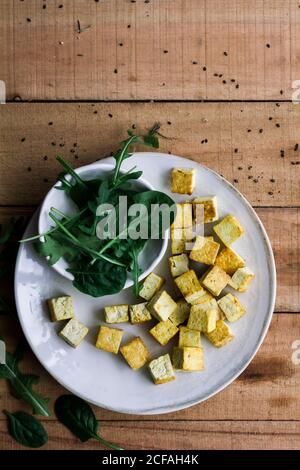 Vista dall'alto di foglie di basilico verde e cubetti di formaggio su piastra su tavola rustica in legno Foto Stock