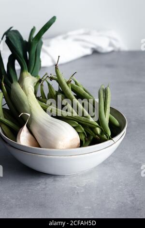 Ciotola bianca con aglio e cipolla verde e fagioli verdi su tavolo in cucina Foto Stock