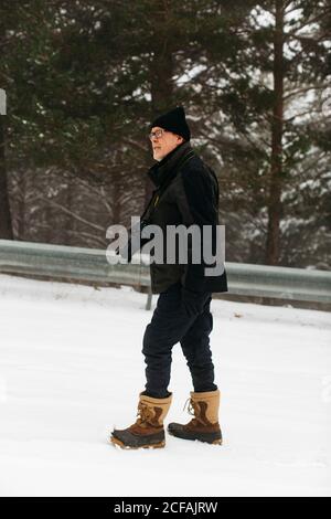 Uomo caucasico anziano che cammina sulla neve per prenderne foto di paesaggi Foto Stock