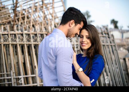 Uomo elegante e donna affascinante in vestito blu abbracciarsi sulla strada lungo le case in ricostruzione Foto Stock