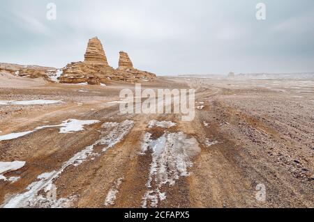 Vecchio edificio di pietra solitario situato tra il deserto nevoso terreno sotto cielo nuvoloso con sole luminoso Foto Stock