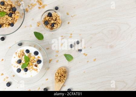 Vista di tre ciotole con muesli, noci, mirtilli e yogurt su una superficie di legno bianco Foto Stock