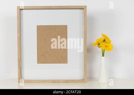 Vista di una cornice da quadro, con tulipani gialli posti in un vaso di vetro su fondo bianco semplice Foto Stock