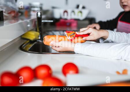 anonimo bambini che peeling carota mentre cucinando insalata sana in cucina Foto Stock