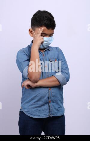 Ragazzo indiano che indossa una maschera chirurgica che si pone su sfondo bianco. Foto Stock