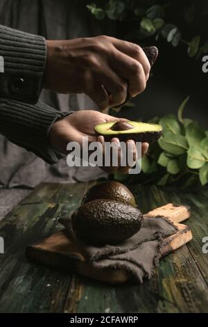 anonima persona mani taglio avocado a metà per preparare guacamole Foto Stock