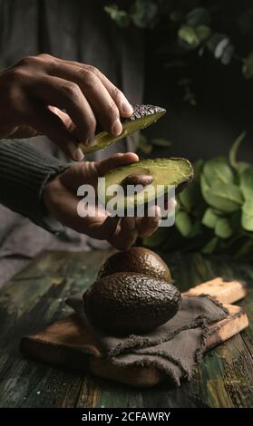 anonima persona mani taglio avocado a metà per preparare guacamole Foto Stock