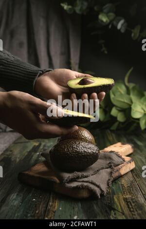 anonima persona mani taglio avocado a metà per preparare guacamole Foto Stock