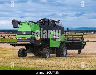 Deustz Fahr Combine Harvesting un campo di grano di orzo in estate con cielo scuro tempestoso, East Lothian, Scozia, Regno Unito Foto Stock