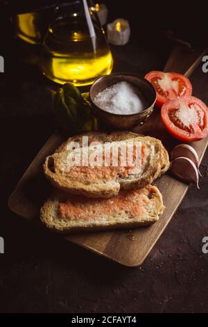 Varie spezie e metà di pomodoro maturo messi al taglio tavola vicino a pezzi di pane con salsa sul tavolo Foto Stock