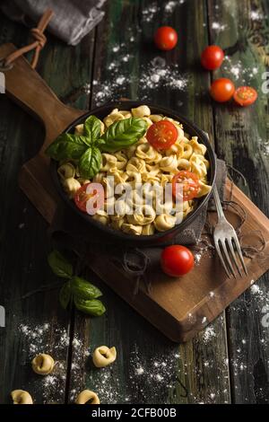 Dall'alto di piatto nero pieno con deliziosi ravioli fatti in casa con pomodori ciliegini tagliati e basilico fresco su taglio di legno tavola posta su tavola di legno Foto Stock