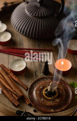 Composizione del cono di incenso e delle candele di tè bruciate su legno vassoio con teiera orientale preparato per il relax e la meditazione Foto Stock