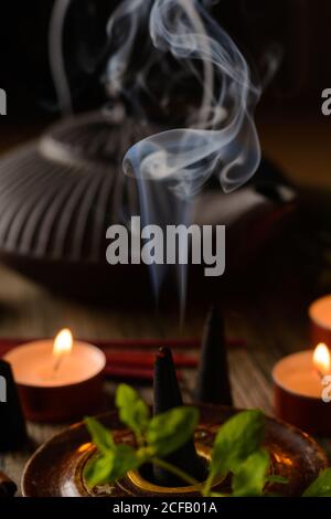 Composizione del cono di incenso e delle candele di tè bruciate su legno vassoio con teiera orientale preparato per il relax e la meditazione Foto Stock