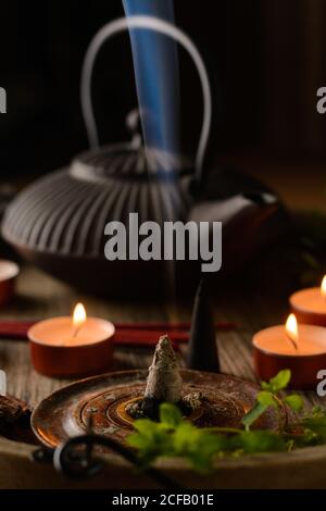 Composizione del cono di incenso e delle candele di tè bruciate su legno vassoio con teiera orientale preparato per il relax e la meditazione Foto Stock