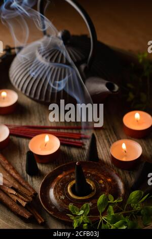 Composizione del cono di incenso e delle candele di tè bruciate su legno vassoio con teiera orientale preparato per il relax e la meditazione Foto Stock