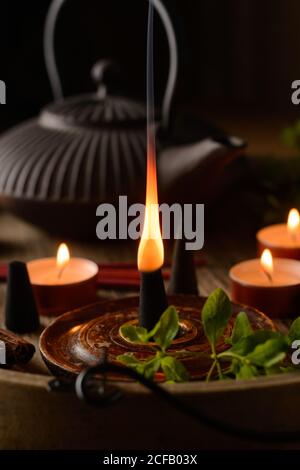 Composizione del cono di incenso e delle candele di tè bruciate su legno vassoio con teiera orientale preparato per il relax e la meditazione Foto Stock