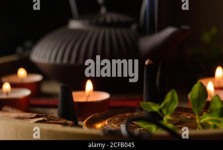 Composizione del cono di incenso e delle candele di tè bruciate su legno vassoio con teiera orientale preparato per il relax e la meditazione Foto Stock