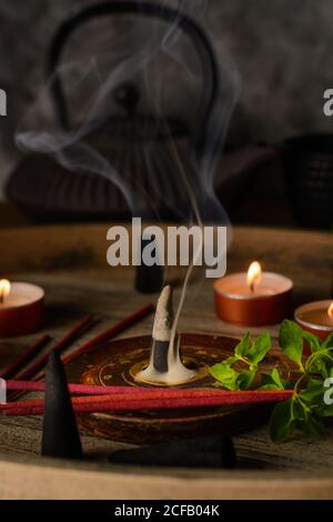 Composizione del cono di incenso e delle candele di tè bruciate su legno vassoio con teiera orientale preparato per il relax e la meditazione Foto Stock