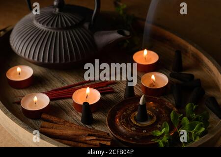 Composizione del cono di incenso e delle candele di tè bruciate su legno vassoio con teiera orientale preparato per il relax e la meditazione Foto Stock