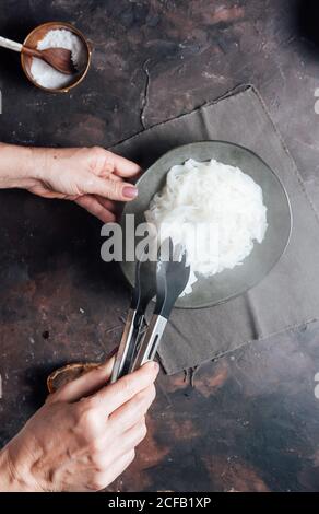 Da sopra raccolto anonimo femmina con pinze da cucina che prendono caldo tagliatelle di riso cotte dalla ciotola mentre si prepara il pranzo in cucina Foto Stock