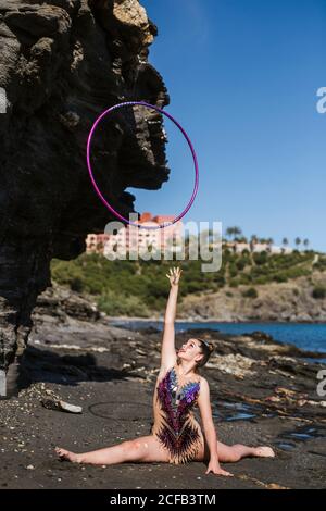 Bella ginnastica femminile seduta su corda e rossiccio su cerchio su sfondo naturale Foto Stock