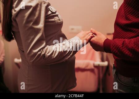 Vista laterale del raccolto donna incinta e marito in piedi nella stanza del bambino di fronte al carrozza del bambino rosa e tenendo le mani Foto Stock