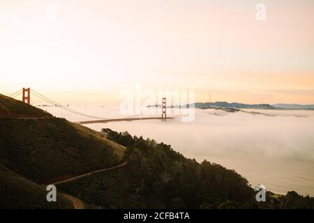 Vista mozzafiato del maestoso Golden Gate Bridge sullo stretto foggoso Tra le spiagge verdi contro il cielo colorato a San Francisco in California durante la calda sera Foto Stock