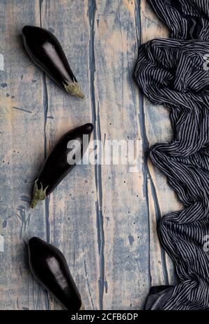 Set di melanzane fresche mature poste vicino a pezzo di striped panno su un piano di lavoro in legno resistente alle intemperie Foto Stock