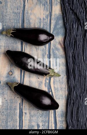 Set di melanzane fresche mature poste vicino a pezzo di striped panno su un piano di lavoro in legno resistente alle intemperie Foto Stock