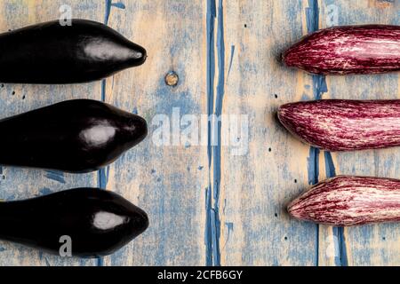 Set di melanzane fresche mature poste vicino a pezzo di striped panno su un piano di lavoro in legno resistente alle intemperie Foto Stock