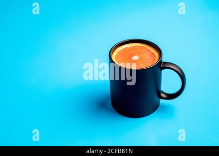 Tazza nera con fetta di agrumi freschi maturi per colazione posizionato su sfondo blu chiaro Foto Stock