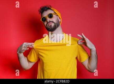 Uomo trendy con bearded in camicia di tenuta gialla in piedi contro Bright sfondo giallo che guarda la fotocamera Foto Stock