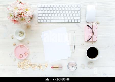 Spazio di lavoro con, computer, carta bianca, crisantemo. Accessori moda donna su sfondo bianco di legno. Riviste, media. Disposizione piatta, vista dall'alto Foto Stock