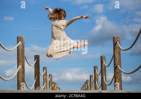 Vista posteriore della giovane ballerina in grigio con colore bianco tessuto in aria sul ponte pedonale e cielo blu in sole giorno Foto Stock